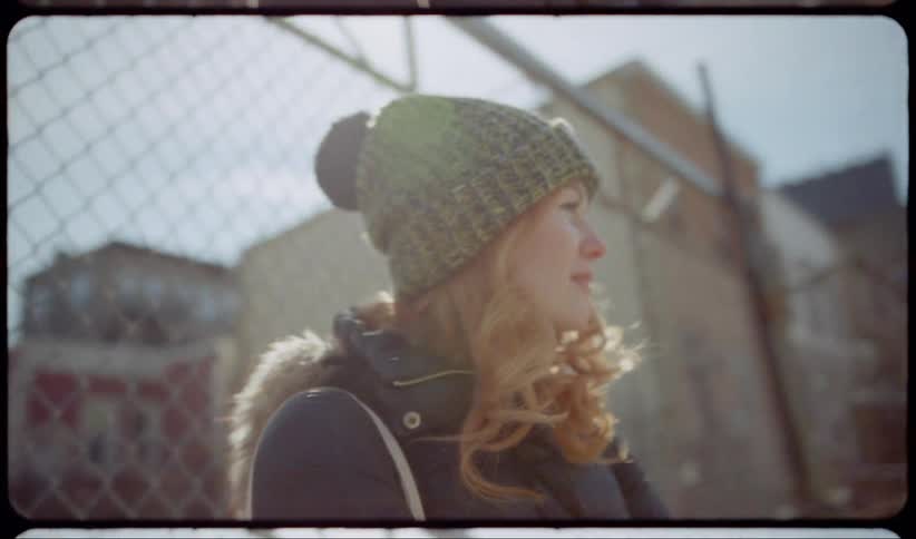 A young woman waiting outdoors near a fence in a city