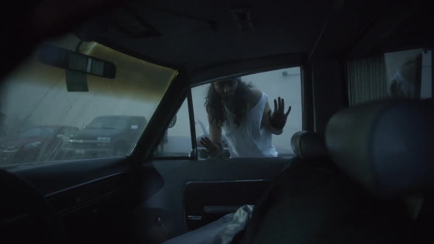 A woman with her hands on the window looks into a car parked in a parking garage