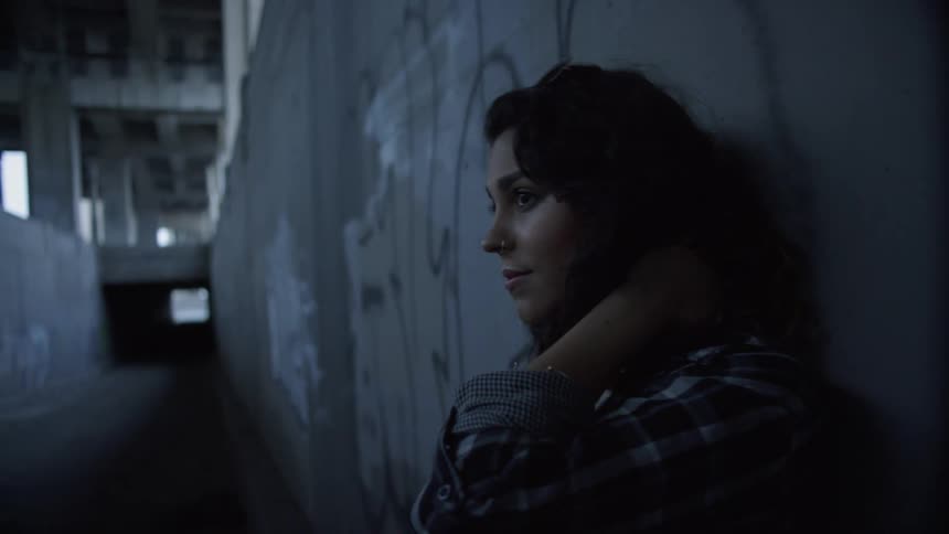 A young woman stands in a hallway and leans against the wall