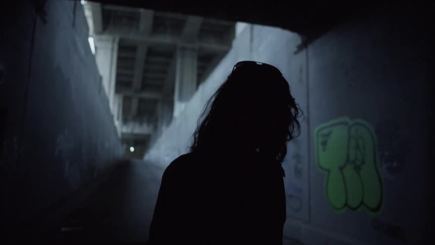 Woman walks down a ramp into a dark tunnel under a bridge