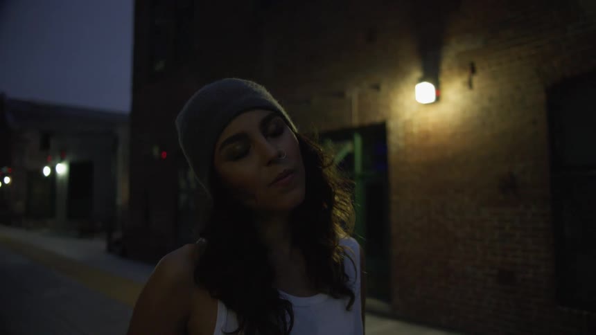 Woman stands in street lined by building lit by outdoor lights at night