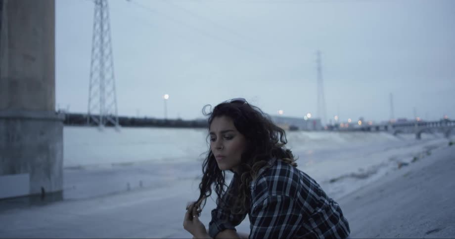 A woman sits outside and looks around while playing with her hair
