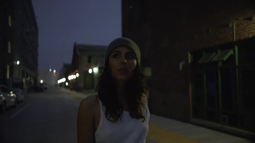 A woman struts down a narrow city street looking around at the buildings