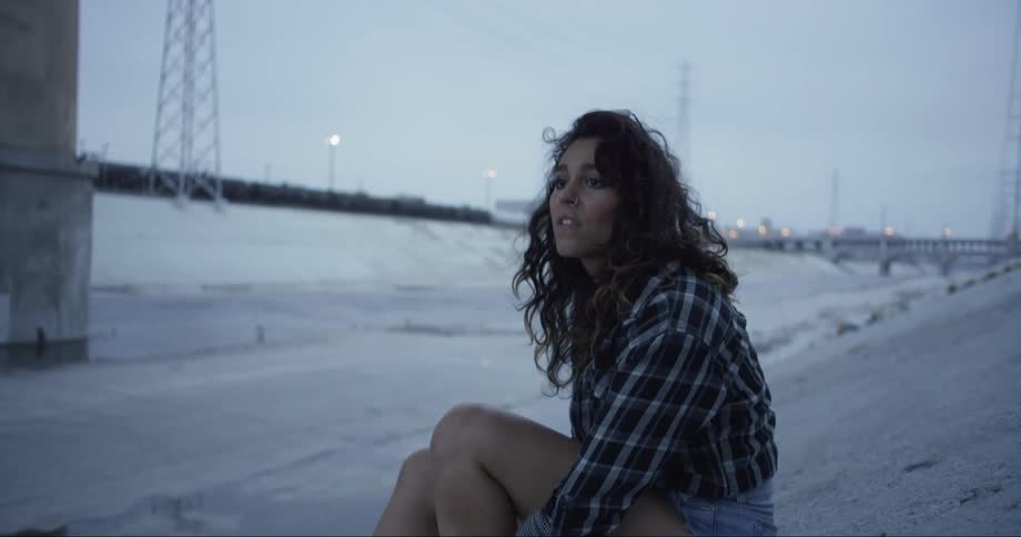 Woman sits on concrete slope under bridge scanning the area