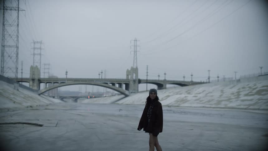 A woman standing outside in a flood control channel the runs beneath a bridge on a snowy day