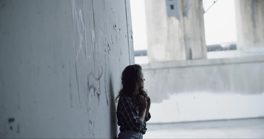 A teenager leans against a concrete wall outside