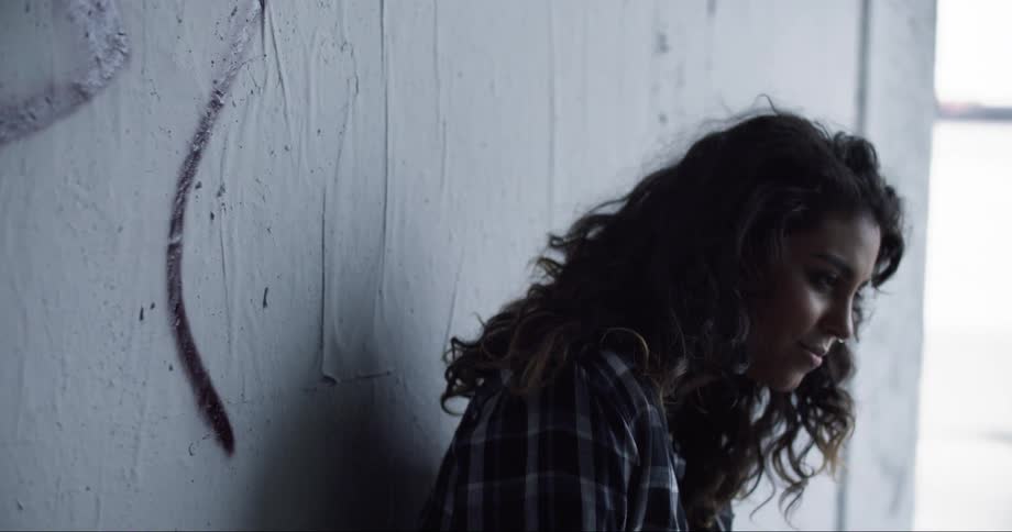 A teenager stands against a wall outside and looks around and smiles