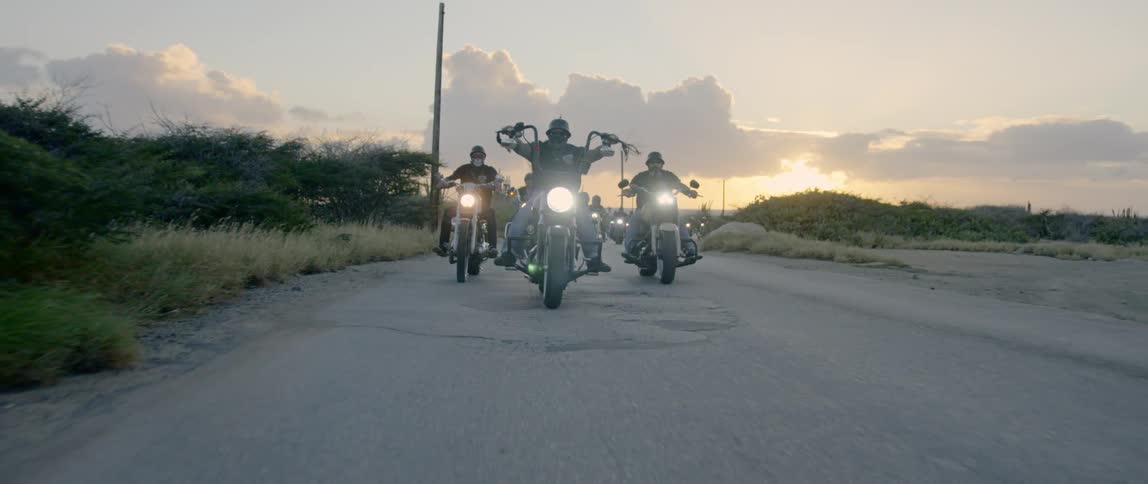 A group of men ride motorcycles down a street