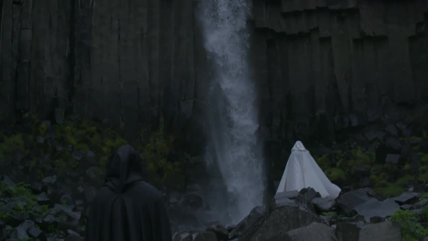 A waterfall is dropping water below as a person wearing white robes watches