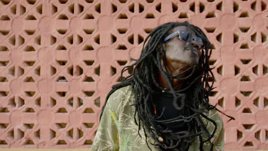 Man tosses his head shaking his braids dancing near wall outdoors