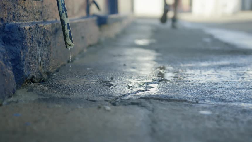 A person walks down a sidewalk with a dripping hose