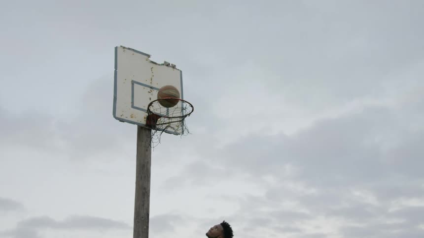 Man shoots a basketball through hoop at sunset