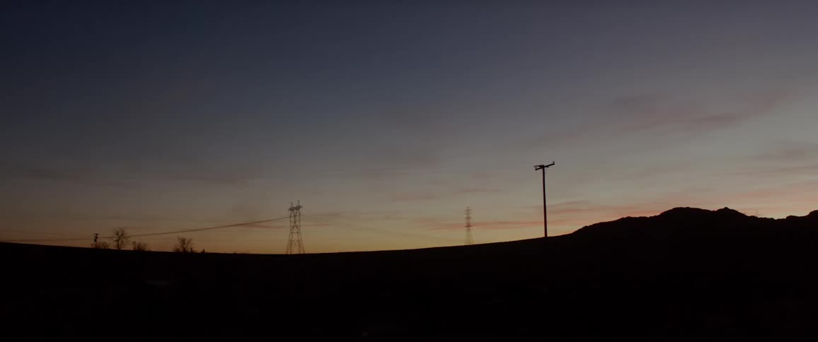 Power poles and trees stand silhouetted against a dawn sky