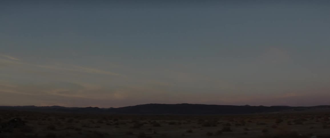 A red sky over a flat field with hills in the far distance
