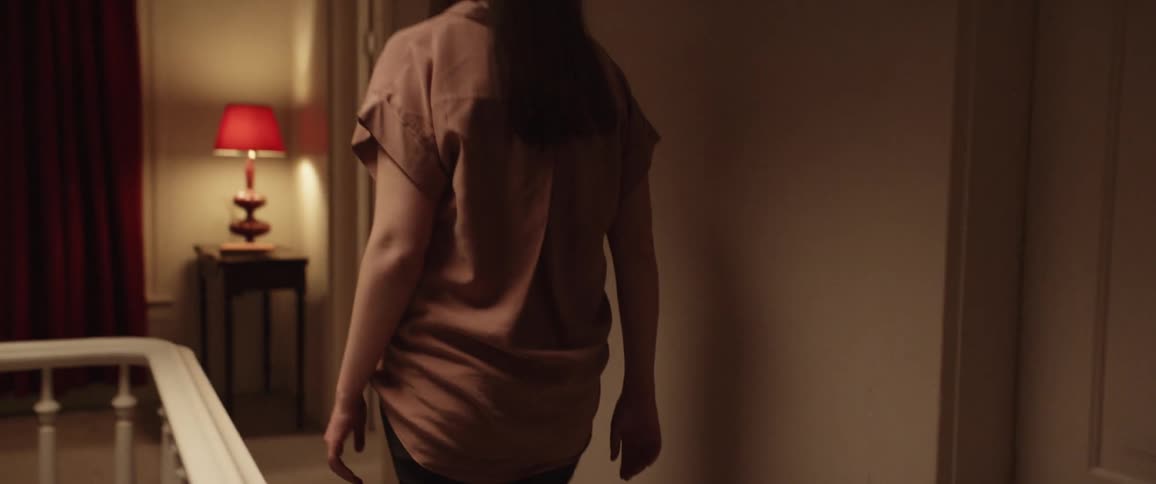 A woman runs her hand along a handrail as she walks down a hallway