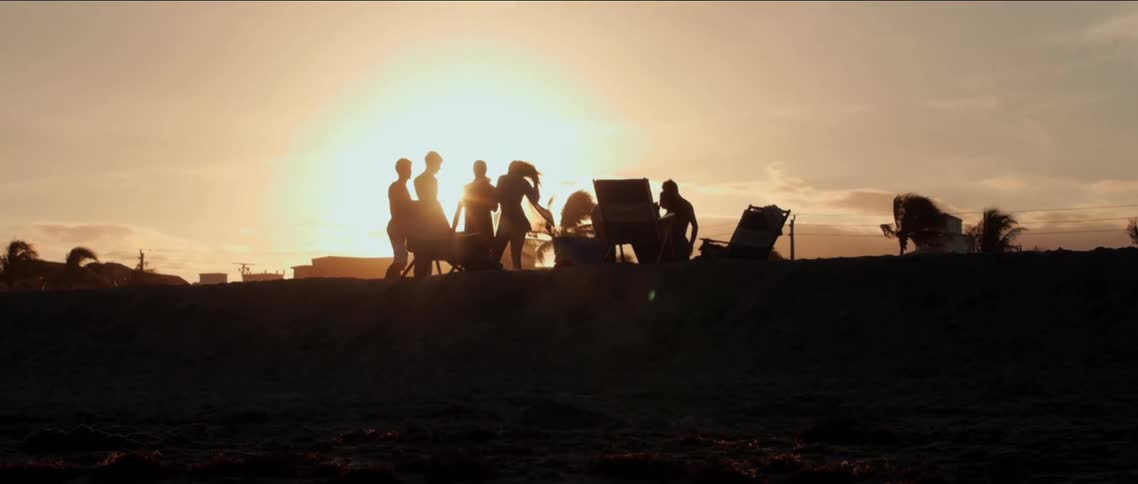 A group of friends gathered with beach chairs above the sand at sunset