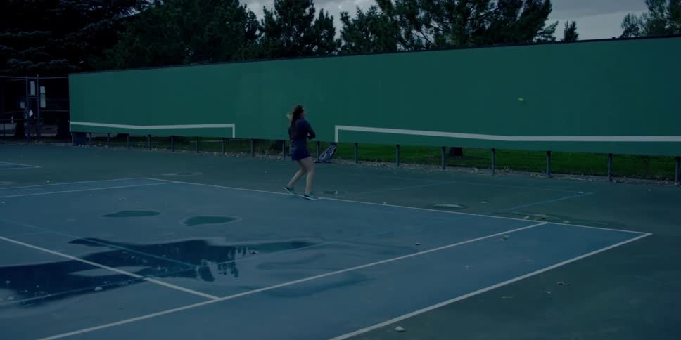 A young white woman practices hitting a tennis ball against a wall