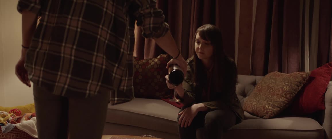 A person pours wine into a womans glass who is sitting on a couch