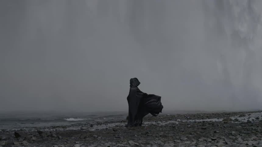A darkly cloaked figure standing on a rocky shoreline