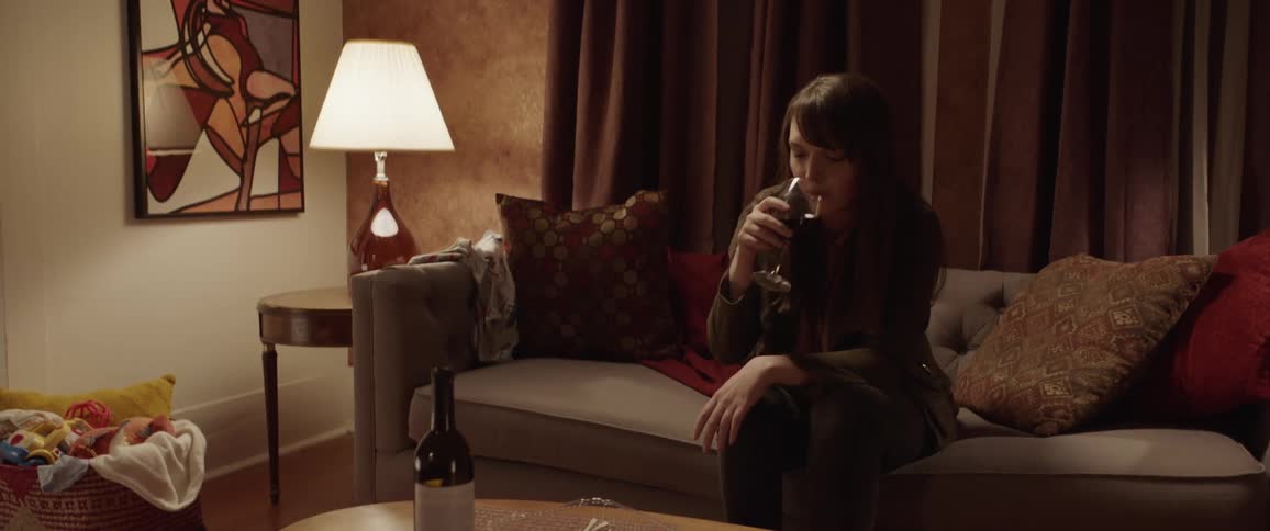 A woman sitting on a couch raises her wine glass in a toast and then takes a drink