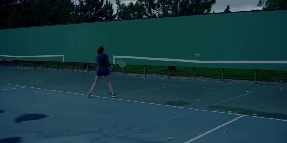 A woman practices her tennis swing alone on a court using the back wall