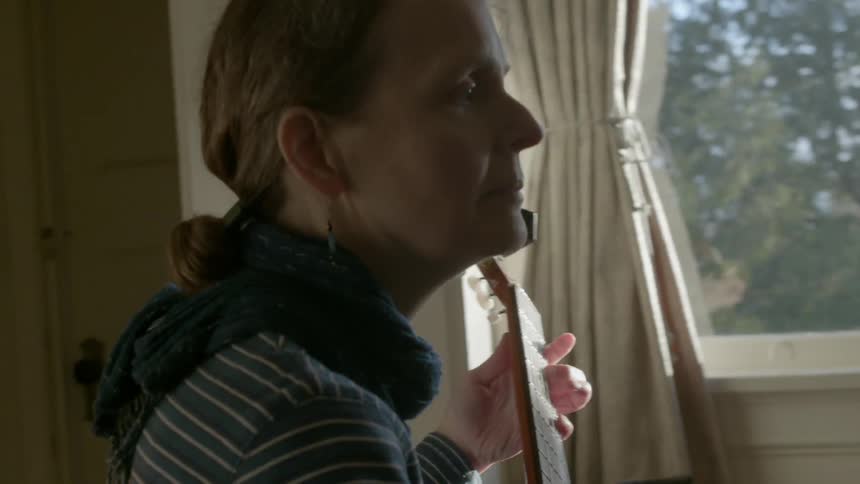A woman is playing an instrument by a window