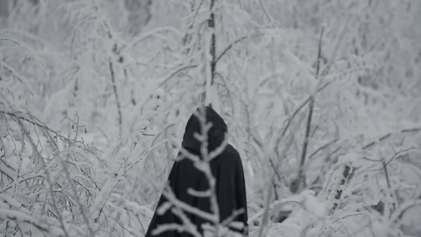 A person wearing black robes is sitting in a snow covered forest