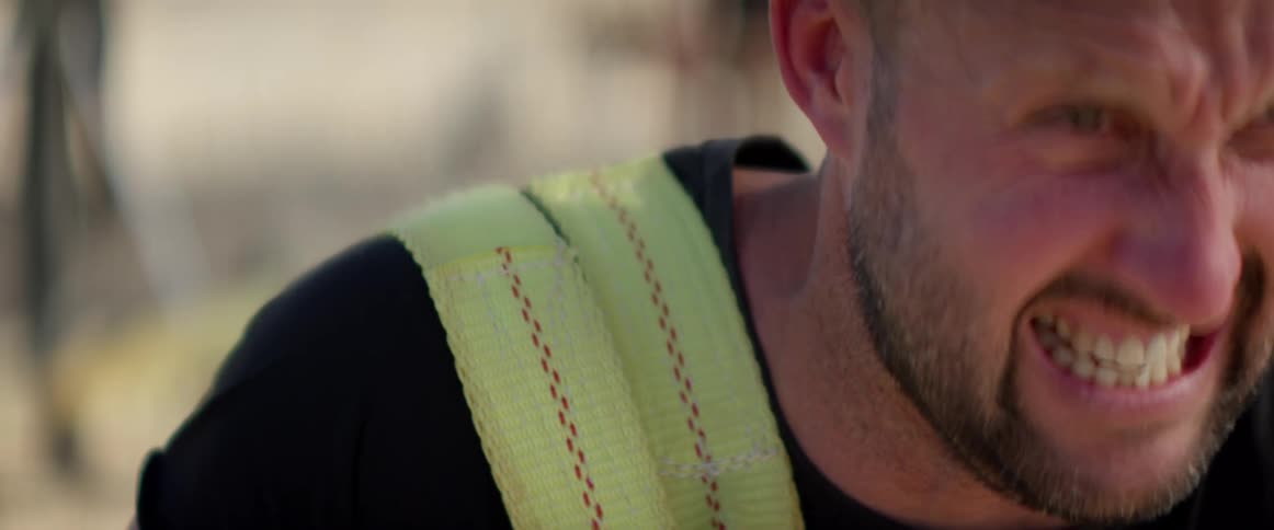 A man holding thick straps uses all his strength to pull something attached to them