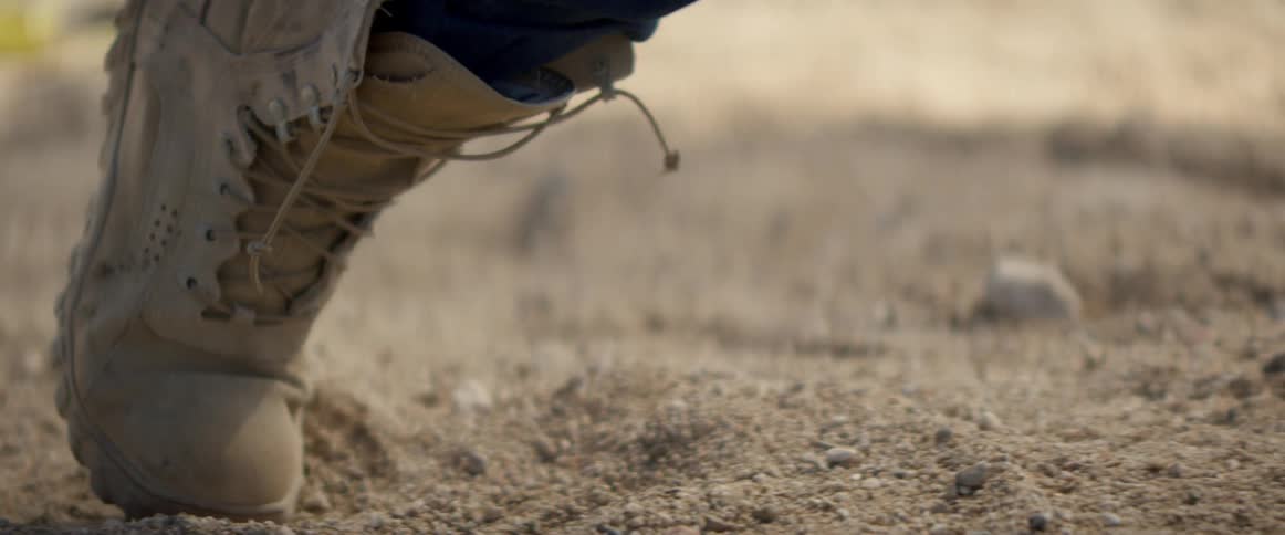 A person in boots is pressing forward in the sand
