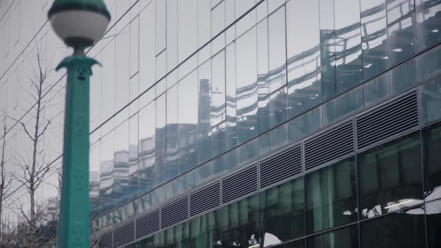 A person walks by a building as a train reflects on it