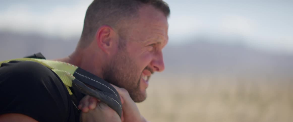 Man grimaces while pulling heavy object with mountains as backdrop