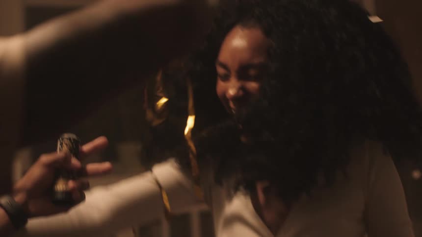 A black woman dances and throws streamers in the living room of a home
