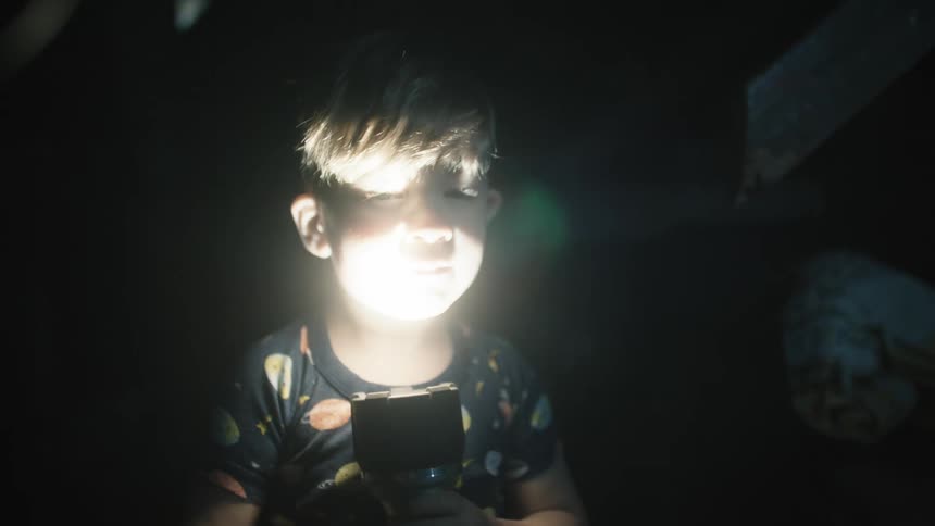 Small kid plays with flashlight in dark room