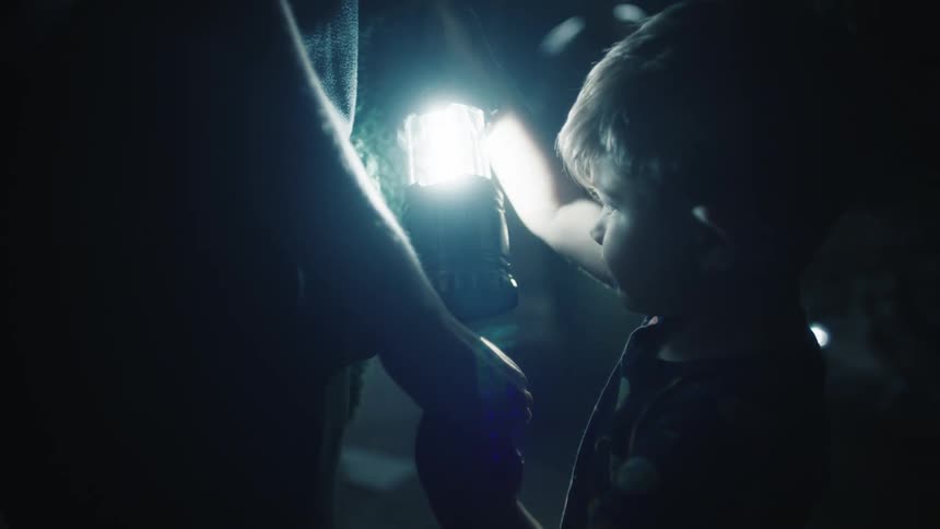 A boy holds a lantern in the dark