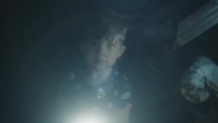 Young boy shines flashlight around while sheltering in dark room