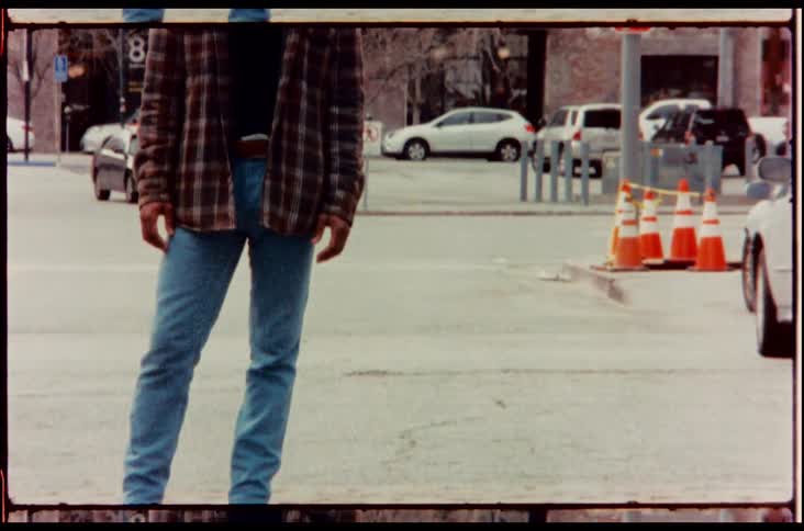 A black man in retro clothing posing on a city street while looking into the camera