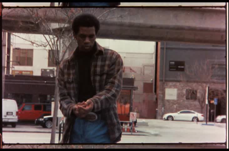 A black man stands in a neighborhood of an urban area