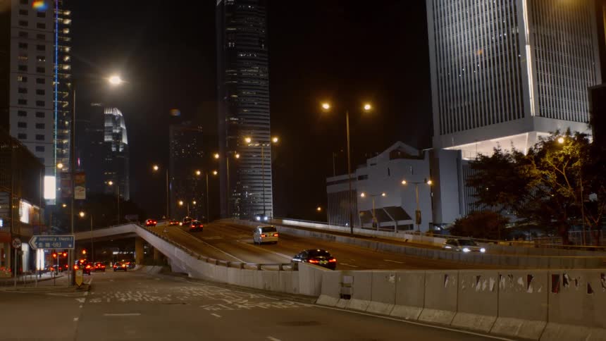 Cars and buses travel on city highway past buildings and over a street below