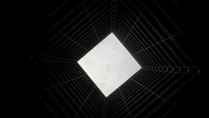Dark walls of building interior lead up to open roof showing cloudy sky