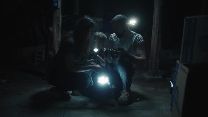 Family crouches in dark room holding flashlights viewing mobile phone