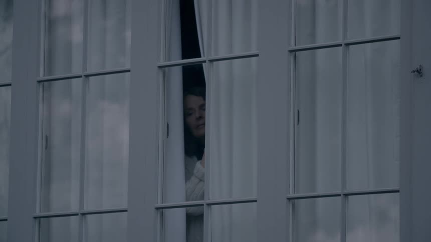A woman pulls back the curtain and peeks outside