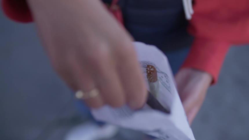A person taking a chocolate covered pretzel stick from a paper bag