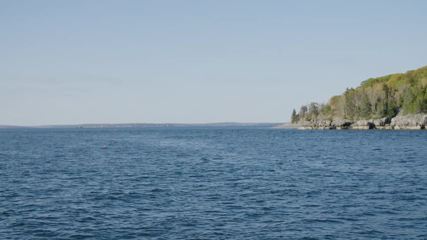 Buoys float on a calm blue ocean near a tree covered rocky shore on a sunny day