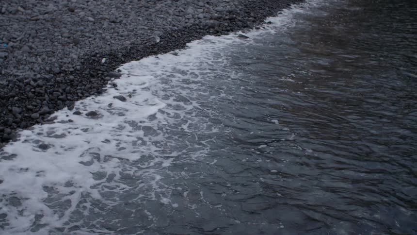 Ocean waves crash against the pebble coast