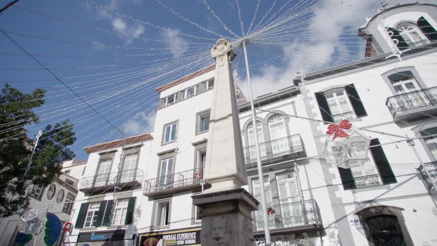 Lights and decorations strung from a pole behind a monument on bright blue sky day