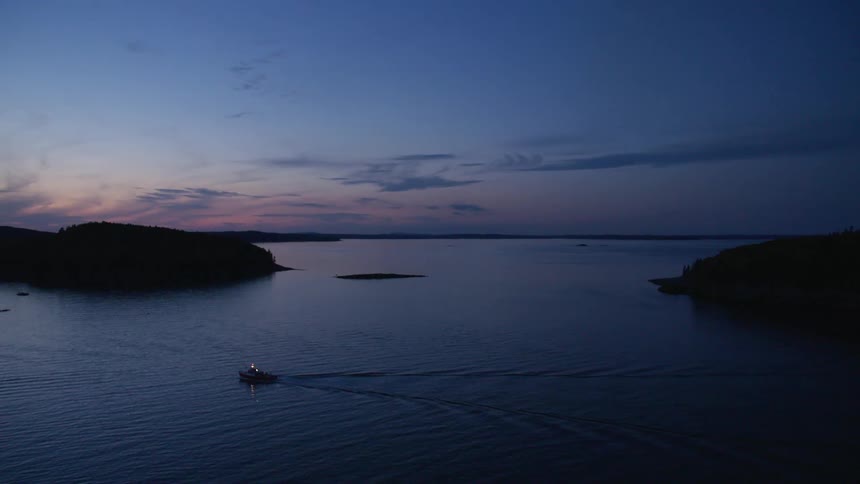 A boat traveling across body of water between land masses at night