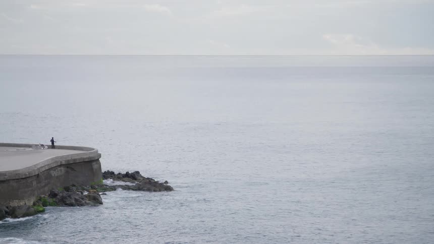 A person stands on a concrete structure next to the ocean