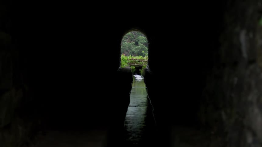 Narrow water way flows through dark tunnel toward park near exit archway