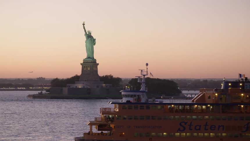 A ferry sails past the statue of liberty at dusk