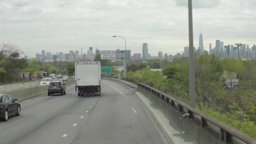 Cars are driving on a highway near a downtown skyline